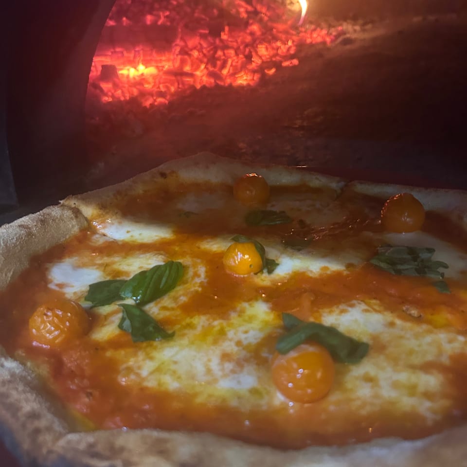 Farina 00 pizza with cherry tomatoes and basil baking in a wood-fired oven.