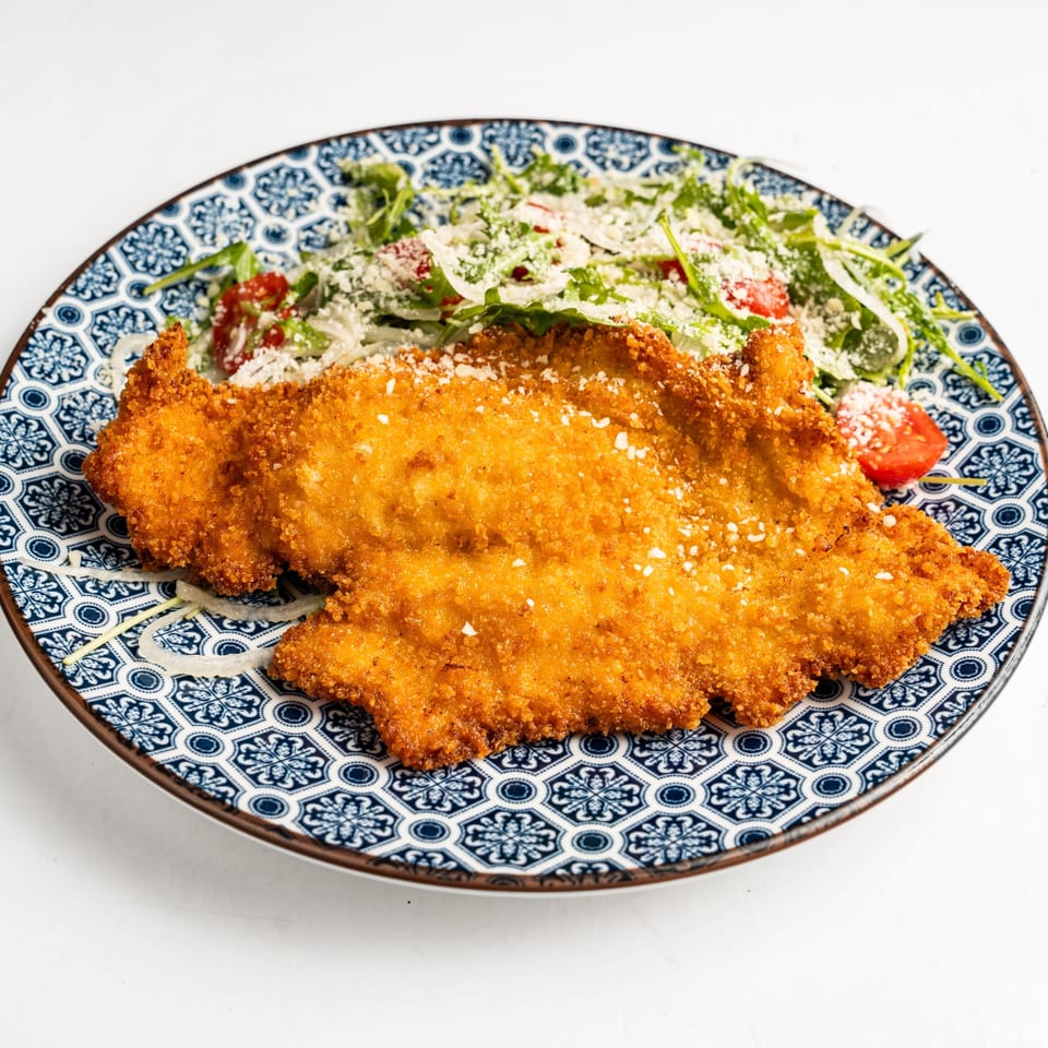 Golden-brown fried chicken cutlet with a side salad of arugula, cherry tomatoes, and grated cheese.