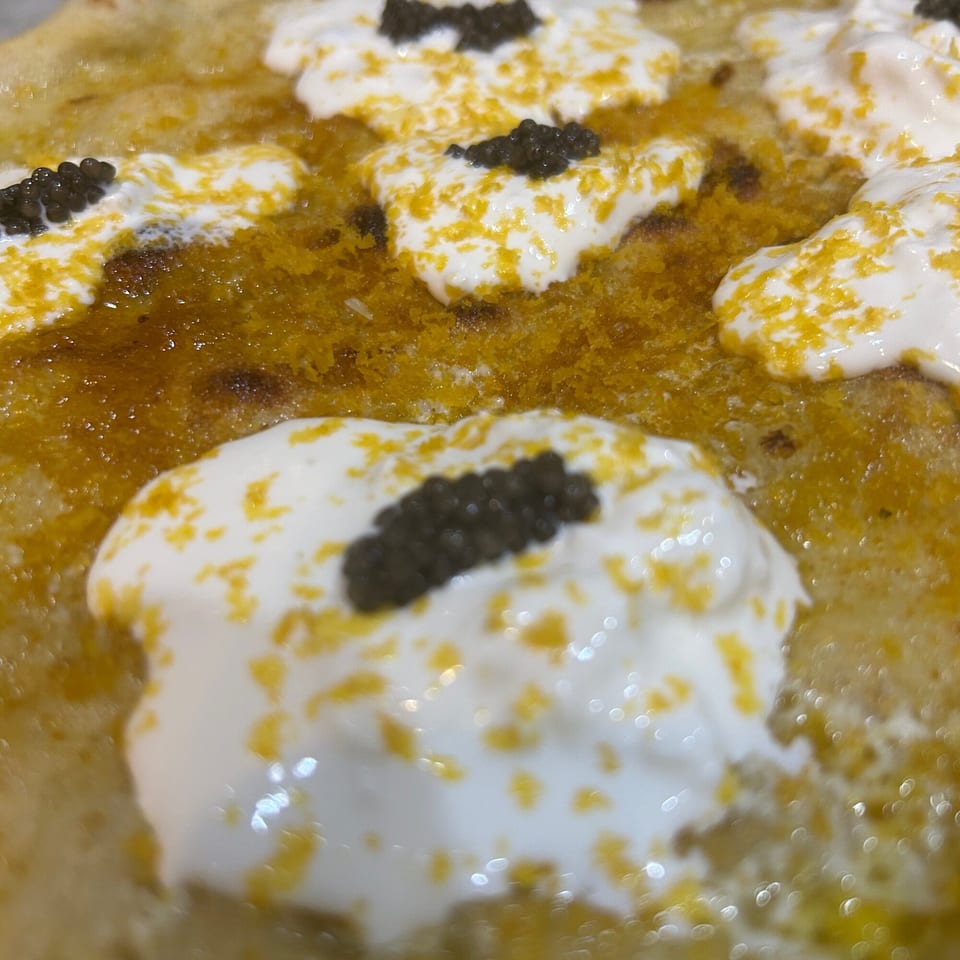 Close-up of a Farina 00 pizza with dollops of white cream, black caviar, and yellow zest.