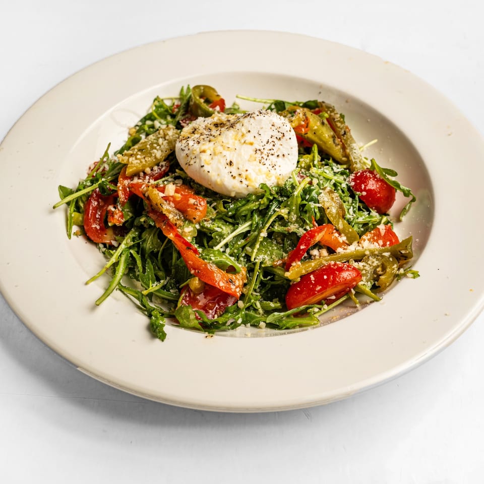 Arugula salad with burrata cheese, roasted red peppers, and green beans in a white bowl.