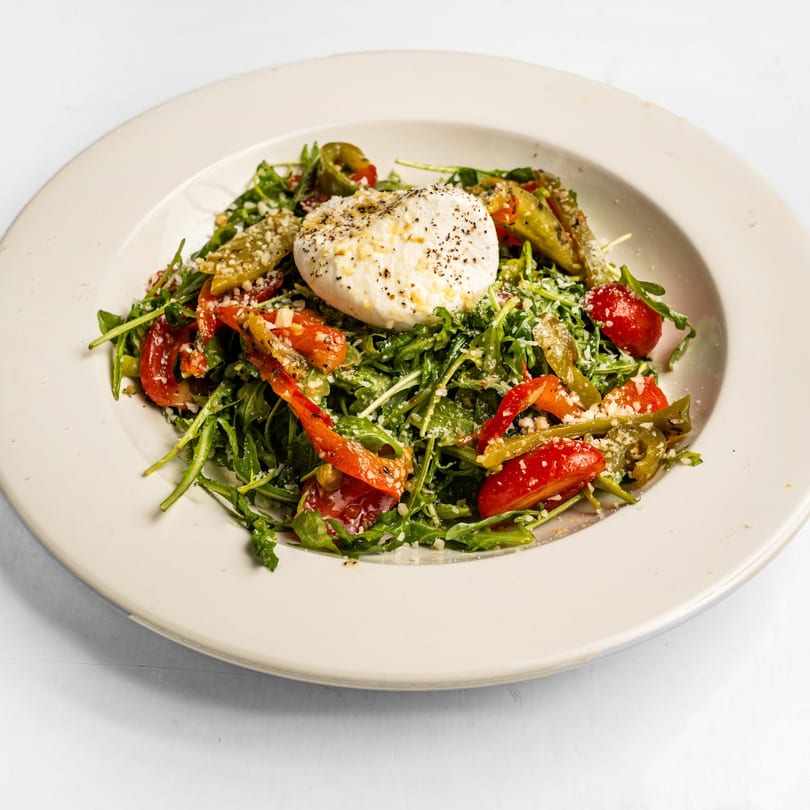 Arugula salad with burrata cheese, roasted red peppers, and green beans in a white bowl.