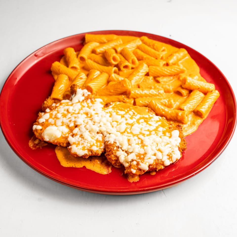 Chicken parmesan with rigatoni pasta in a creamy orange sauce, served on a red plate.