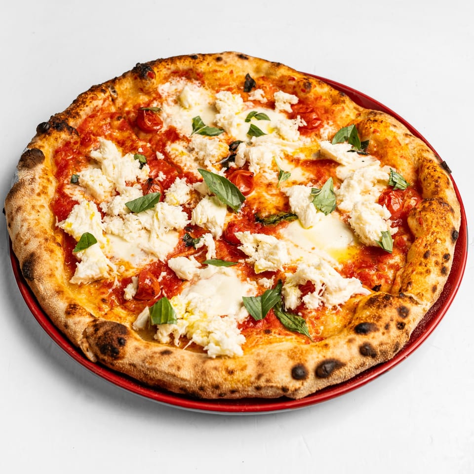Neapolitan pizza with tomato sauce, ricotta cheese, roasted cherry tomatoes, and fresh basil on a red plate.