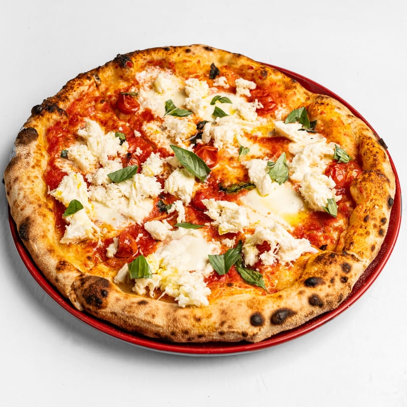 Neapolitan pizza with tomato sauce, ricotta cheese, roasted cherry tomatoes, and fresh basil on a red plate.